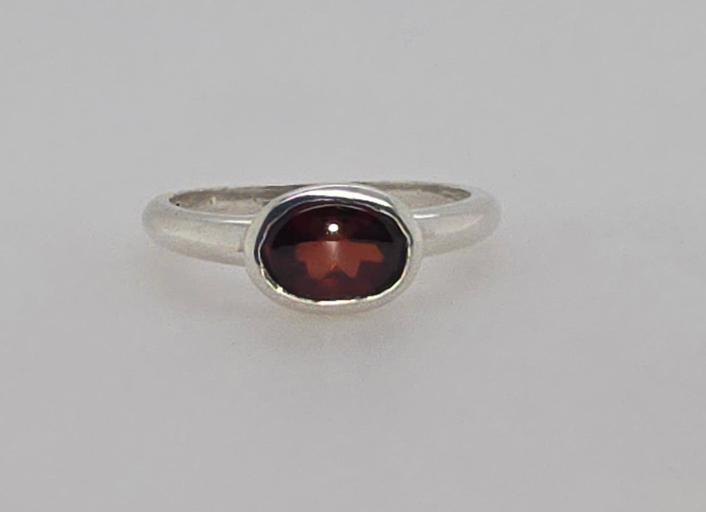 STERLING SILVER BEZEL SET 8 X 6 OVAL GARNET RING.